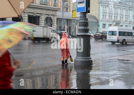 A Straße Reiniger trägt eine helle orange Regenjacke in einer verregneten Straße in Moskau Stockfoto