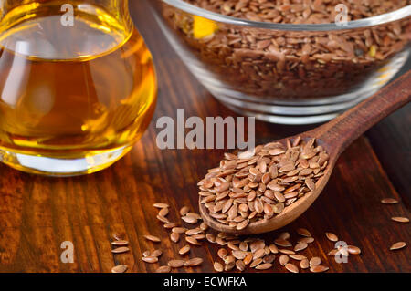 Brauner Leinsamen auf Löffel und Leinsamen Öl in Glaskanne auf Holztisch. Leinöl ist reich an Omega-3-Fettsäure. Stockfoto