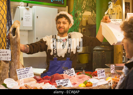 Christmas at Borough Market, London UK - Fischverkäufer in festlichem Outfit, trägt Weihnachtspullover und Weihnachtsmütze, verkauft Fisch am Stand im Dezember Stockfoto