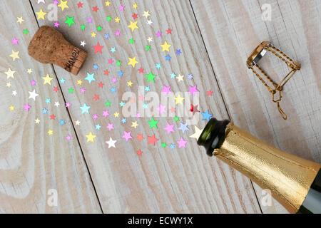 Aufwand für eine Flasche Champagner mit dem Korken knallend auf einem rustikalen Holztisch. Das Spray aus der Flasche ist Stars der verschiedenen si Stockfoto
