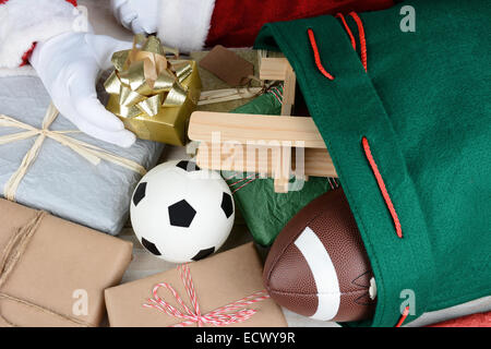 Nahaufnahme von Santa Claus seine Tasche mit Spielzeug und Geschenke zu füllen. Nur Santas Hände sind sichtbar. Verpackte Geschenke Fußball Stockfoto