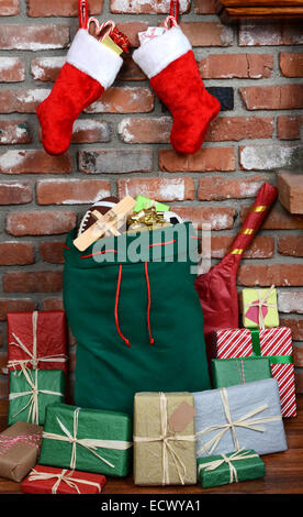 Santa Claus Tasche stützte sich auf die Ziegel eines Foyers. Die Tasche ist gefüllt mit Spielzeug und umgeben von verpackte Geschenke. Stockfoto