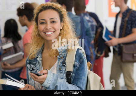 Lächelnde Studentin mit Handy, mit anderen Studenten im Hintergrund Stockfoto