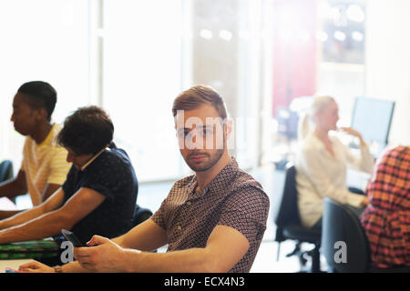 Männliche Schüler sitzen am Schreibtisch im Klassenzimmer und mit Handy Stockfoto