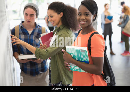 Studentin, lächelnd in die Kamera mit zwei anderen Studenten am schwarzen Brett Stockfoto