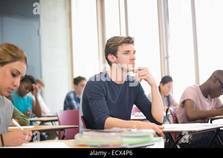 Männliche Schüler mit Hand am Kinn während der Vorlesung mit anderen Studenten im Hintergrund Stockfoto