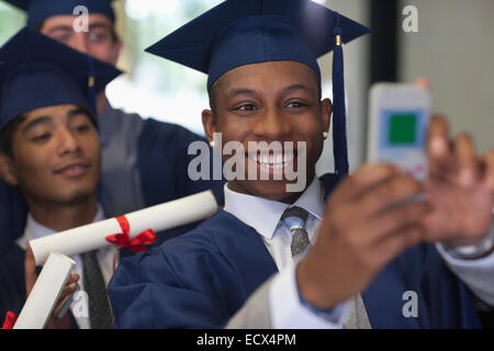 Lächelnd männlichen Studenten tragen Graduierung Kleider nehmen Selfie mit Freunden Stockfoto