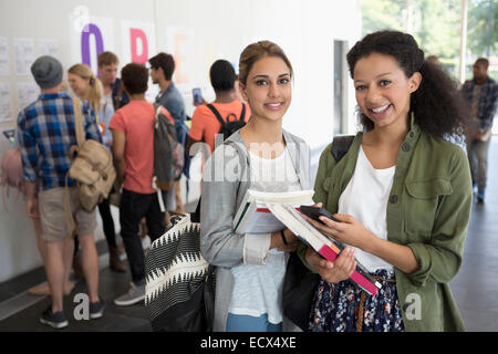 Porträt von zwei Studentinnen, die mit Büchern, anderen Studenten im Hintergrund lächelt Stockfoto