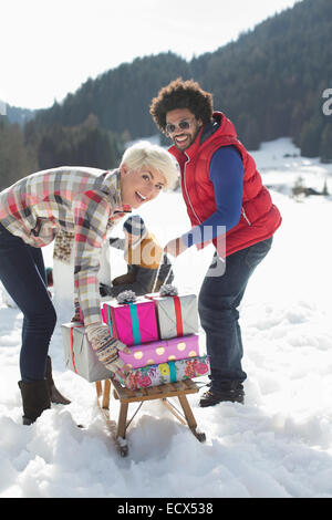 Porträt des Paares mit Schlitten und Weihnachtsgeschenke im Schnee Stockfoto