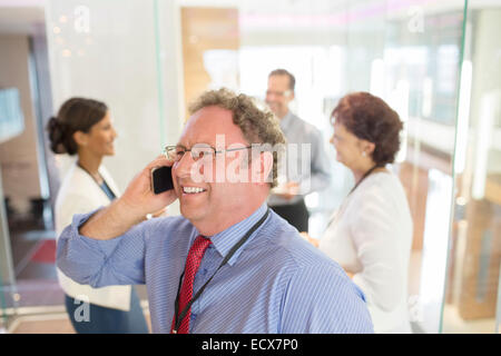 Telefonieren mit Handy, Kolleginnen und Kollegen im Hintergrund stehen Geschäftsmann Stockfoto