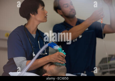 Arzt Holding Sauerstoffmaske über Patient, Arzt, die Anpassung der Tropf auf Intensivstation Stockfoto