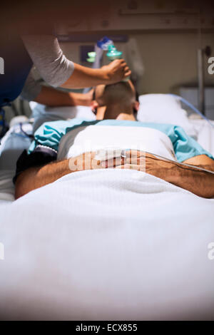 Krankenschwester mit Sauerstoffmaske über männliche Patientenmund auf Intensivstation Stockfoto