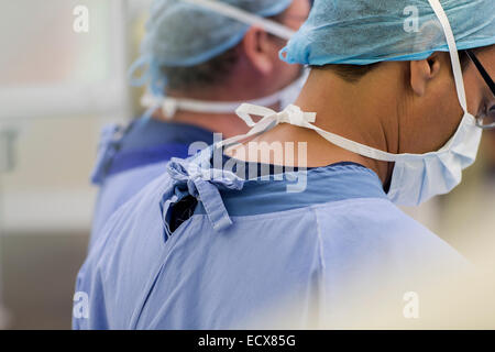 Ärzte tragen chirurgische Mützen, Masken und Peelings im Operationssaal Stockfoto