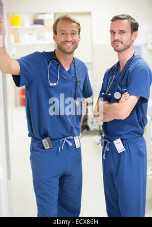 Zwei männliche Ärzte tragen lächelnd Scrubs – Die Anfänger stehen im Krankenhaus Stockfoto