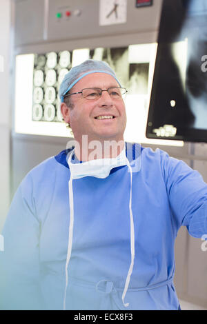 Lächelnde Reife Arzt chirurgische Kleidung Blick auf Röntgen im Krankenhaus Stockfoto