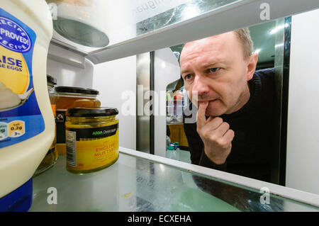 Man sieht in einem Kühlschrank mit einem erstaunten Blick auf seinem Gesicht. Stockfoto