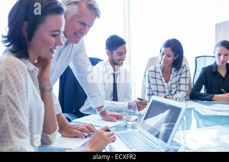 Unternehmerinnen und Unternehmer am Konferenztisch sitzen, mit Laptop und lächelnd Stockfoto