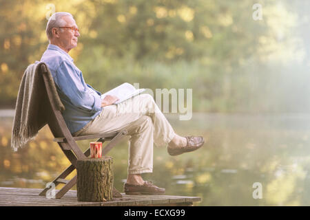 Älterer Mann Buch auf Dock am See Stockfoto