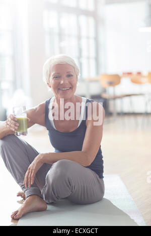 Ältere Frau trinken Saft auf Gymnastikmatte Stockfoto