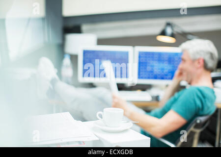 Geschäftsmann lesen Papierkram im Büro hinter Kaffeetasse Stockfoto