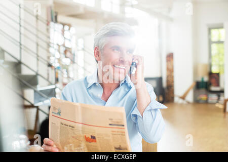 Älterer Mann reden über Handy mit Zeitung Stockfoto