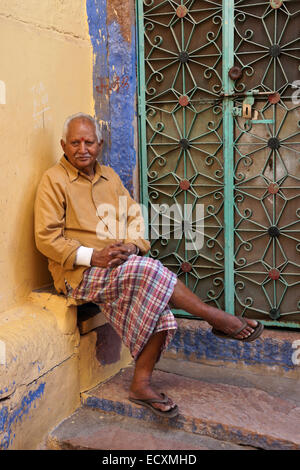 Alter Mann sitzt vor seinem Haus in die blaue Stadt Jodhpur, Rajasthan, Indien Stockfoto