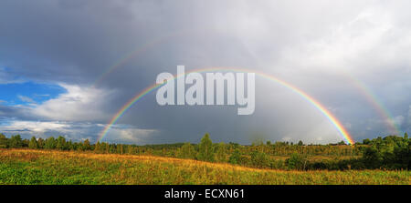 Ein helle doppelter Regenbogen wölbt sich über einem Dorf. Stockfoto