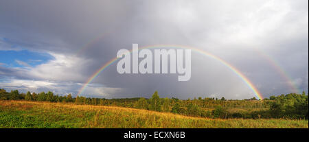 Ein helle doppelter Regenbogen wölbt sich über einem Dorf. Stockfoto