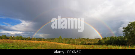 Ein helle doppelter Regenbogen wölbt sich über einem Dorf. Stockfoto