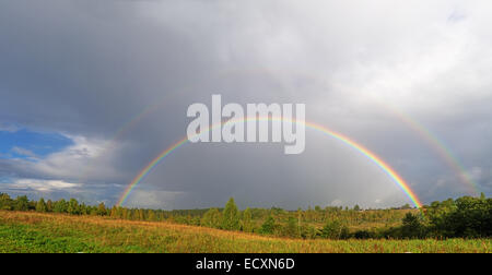 Ein helle doppelter Regenbogen wölbt sich über einem Dorf. Stockfoto