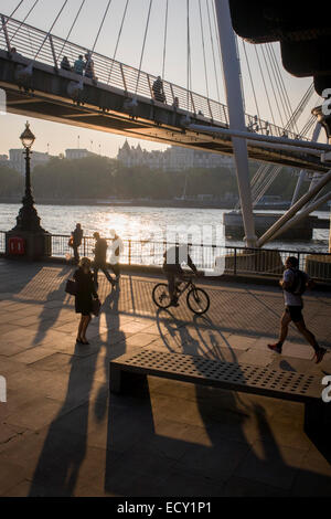 Silhouetten von Pendlern Hungerford Bridge überqueren und der Wanderer am Themse-Ufer. Stockfoto