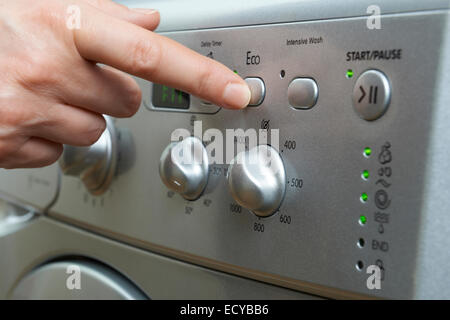 Frau Wahl Wirtschaft Programm auf Waschmaschine um Energie zu sparen Stockfoto