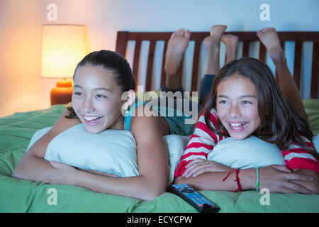 Gemischte Rassen Schwestern vor dem Fernseher auf Bett Stockfoto