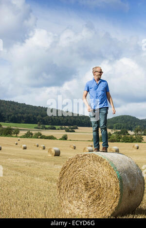 Bauer auf Heuballen im Feld stehen Stockfoto