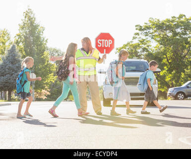 Kaukasische Crossing Guard Hilfe für Kinder in Zebrastreifen Stockfoto