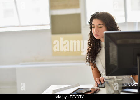 Gemischte Rassen Geschäftsfrau mit Handy und Computer am Schreibtisch im Büro Stockfoto