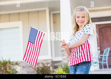 Lächelnd kaukasische Mädchen wehenden amerikanischen Flagge in der Nähe von Haus Stockfoto