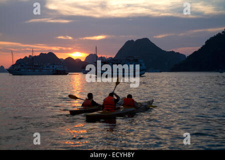 Touristen mit Seekajaks bei Sonnenuntergang in Ha Long Bucht, Vietnam. Stockfoto