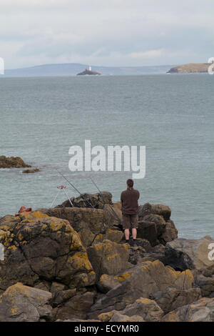 Mann Angeln auf Felsen am Porthgwidden Beach, St. Ives, Cornwall mit Godrevy Leuchtturm in Ferne Stockfoto