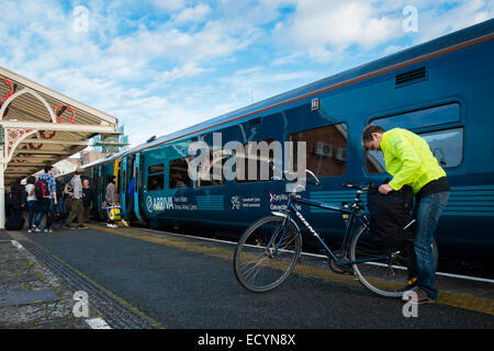 Ein Frau Radfahrer prüft ihr Fahrrad vor dem Einsteigen in eines Arriva Trains Wales Zuges am Bahnhof von Aberystwyth, Wales UK Stockfoto