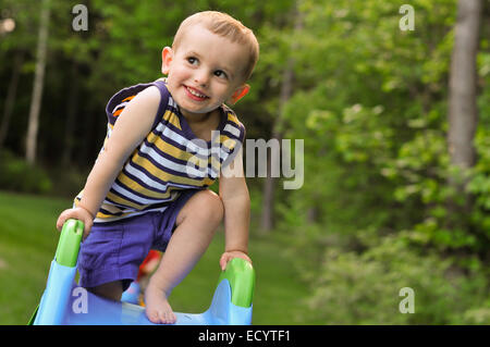 Ein Kleinkind-junge in ein gestreiftes Tank-Top spielt auf einer Kunststoff-Folie im Sommer. Stockfoto