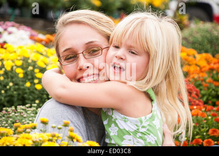 20er Jahre Frau wird umarmt von einem 2 Jahre alten Mädchen.  Es gibt viele Blumen in Out-of-Fokus-Hintergrund. Stockfoto