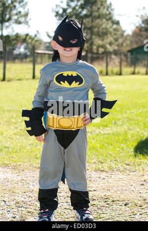 ca. 4-5 Jahre alter Junge in einem Batman-Kostüm.  Die Gesichtsmaske ist krumm.  Er steht mit einer Hand an der Hüfte.  Er ist draußen.