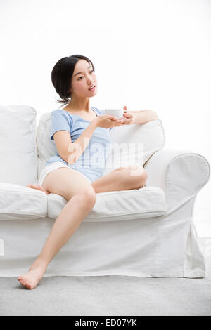 Junge Frau trinkt Kaffee auf sofa Stockfoto