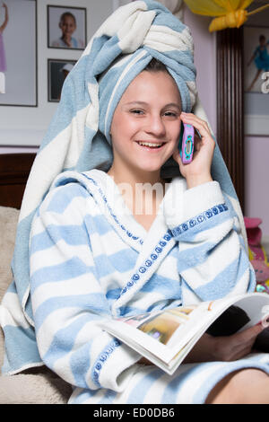 Mädchen im Morgenmantel telefonieren während des Lesens Magazin Stockfoto