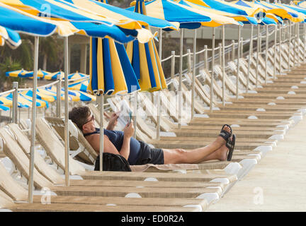 Mann liest Zeitung auf der Sonnenliege am Strand in Spanien Stockfoto