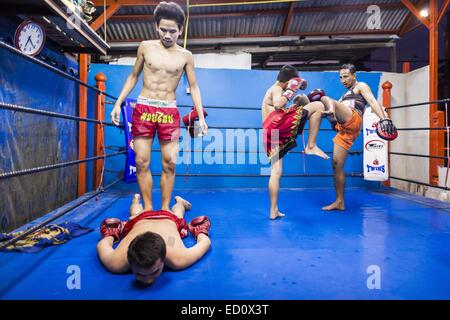 Bangkok, Thailand. 23. Dezember 2014. Ein Boxer hilft ein weiterer Kämpfer Knicke aus seinem Rücken zu bekommen, während andere Boxer in den Ring in der Turnhalle Kanisorn Holm. Die Kanisorn-Box-Gym gibt einen kleinen Fitnessraum entlang der Wong Wian Yai - Samut Sakhon Bahngleisen. Junge Menschen aus den umliegenden Gemeinden kommen in die Turnhalle, Thai-Boxen zu lernen. Muay Thai (Muai Thai) ist eine gemischte Kampfkunst in Thailand entwickelt. Muay Thai wurde international im zwanzigsten Jahrhundert, als Thai-Boxer andere bekannte Boxer besiegt weit verbreitet. Eine professionelle Liga richtet sich nach der World Muay Thai Council. Stockfoto