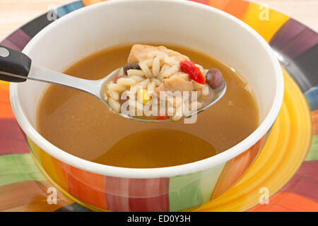 Nahaufnahme von einem Löffel Reis, Huhn, Paprika, Mais und schwarzen Bohnen mit dem Rest der Suppe in eine Schüssel geben. Stockfoto