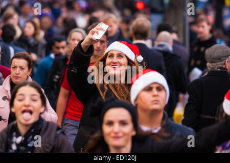 London, UK. 23. Dezember 2014. Von Händlern als die "Goldene Stunde" betitelt verwenden Tausende von Käufern ihrer Mittagspause um zu tun, einige Last-Minute-Weihnachts-shopping im Londoner West End. Bild: Eine Frau nimmt eine Selfie, wie sie und Tausende andere ihren Weg entlang der Oxford Street. Bildnachweis: Paul Davey/Alamy Live-Nachrichten Stockfoto