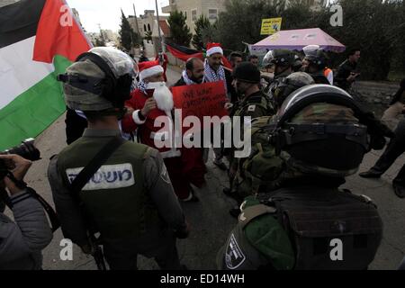 Bethlehem. 23. Dezember 2014. Palästinensische Demonstranten Weihnachtsmann Kostüme tragen Zusammenstoß mit israelischen Soldaten in einem israelischen Checkpoint in der West Bank von Bethlehem am 23. Dezember 2014. Der Protest soll Nachfrage freien Zugang nach Jerusalem in den Weihnachtsferien. © Luay Sababa/Xinhua/Alamy Live-Nachrichten Stockfoto